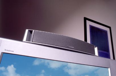 Enceinte centrale Bose VCS10 argentée, vue de face et de côté, sur fond bleu ciel avec nuages blancs
