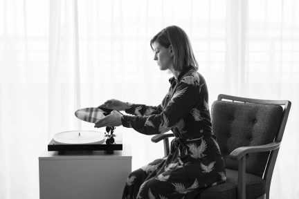 Siddende kvinde lægger en vinylplade på en hvid pladespiller, set i profil