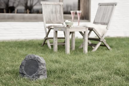 enceinte Bluetooth de jardin en forme de rocher gris sur pelouse devant salon de jardin en bois