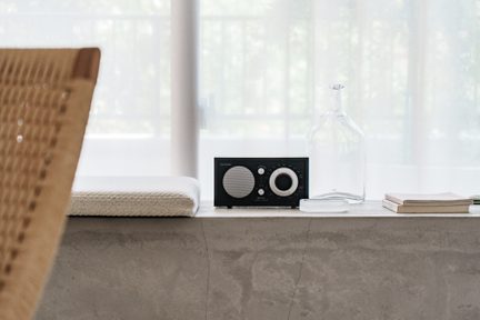 Črna namizna radijska postaja Tivoli Audio v vintage slogu na betonski okenski polici v minimalističnem interierju