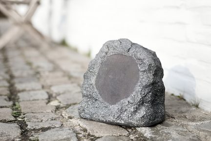 Enceinte Bluetooth d’extérieur gris pierre imitant un rocher, grille ronde apparente, posée sur terrasse en pavés