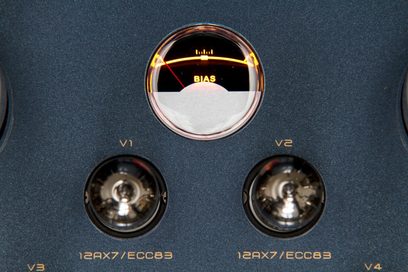 Primo piano dall’alto della piastra superiore argentata in metallo spazzolato dell’amplificatore integrato stereo a valvole Cayin CS-55A EL34, che mostra un vu-meter circolare retroilluminato BIAS e due valvole 12AX7/ECC83 etichettate V1 e V2