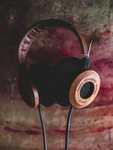 Åben hi-fi hovedtelefon Grado GS1000e i lyst træ, set fra en trekvartvinkel forfra, liggende på en mørkerød, tekstureret stofoverflade