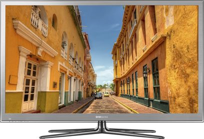 Samsung PS64D8000 tv-skærm, der viser en brolagt gade med farverige bygninger under en blå himmel