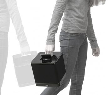 Arcam Solo RCube sort multimedie-højttaler, set forfra, holdt i en hånd i højre side, med grå jeans i baggrunden