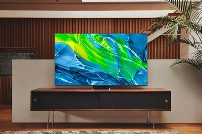 Samsung QE65S95B 2022 fladskærms-TV, der viser et abstrakt billede af grønne og blå former på et mørkt træmøbel
