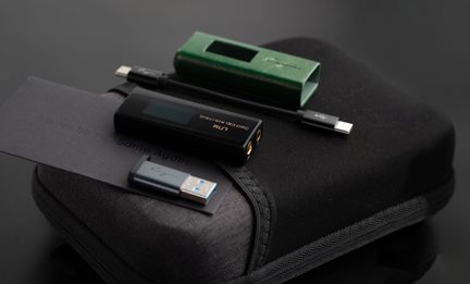 Let letbillede af en lille, sort, rektangulær DAC i metal med skærm og dobbelte gyldne hovedtelefonudgange, ledsaget af en gennembrudt, metallisk grøn manchet, et kort sort USB-C-kabel, en tofarvet USB-A-adapter og et hårdt etui i sort stof