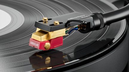 Nærbillede, sidevisning af en rød og gylden phono-pickup i metal og plast på sort vinylplade, tonearm