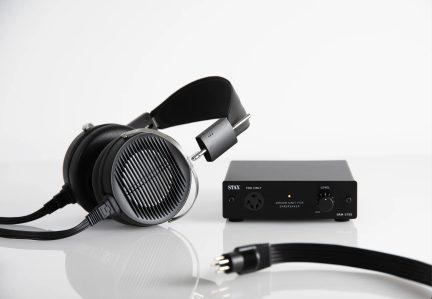 Black headphones with metal grille, black amplifier with buttons and connectors, black 5-pin cable