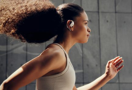 Weiße kabellose Sport-Ohrhörer mit Ohrbügel, getragen von einer Läuferin im beigen Sport-BH im Profil