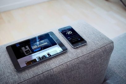 Subwoofer SVS PB-2000 Pro v černém provedení ash položený na šedé tkanině, se smartphonem a tabletem zobrazujícími nastavovací aplikaci