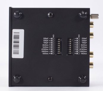 Передпідсилювач фонокоректора Pro-Ject Phono Box S2 сріблястого кольору, вид ззаду, прямокутний чорний корпус, 4 круглі ніжки, 2 DIP-перемикачі, білі написи, позолочені RCA-роз'єми справа, етикетка зі штрих-кодом зліва
