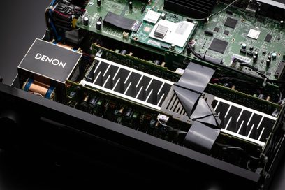 Innenansicht eines schwarzen Denon AVC-X3800H-Verstärkers, die die Leiterplatte mit Komponenten, Kühlkörpern und Lüftern zeigt