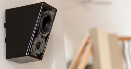 Svart väggmonterad högtalare med vinklad design, med bas- och diskantelement tydligt synliga i närbild