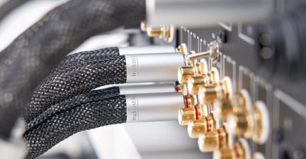 Sorte flettede audiokabler med sølvfarvede metalstik forbundet til guldbelagte terminaler på et elektronisk panel