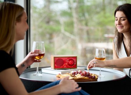 Radio in legno da tavolo con frontale rosso, altoparlante rotondo e grande pulsante, vista frontale su un tavolo con bicchieri e vassoio