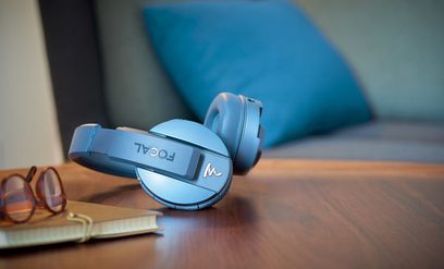 Otvorené hi-fi slúchadlá Focal Listen Chic Wireless v modrej farbe, pohľad z ľavého profilu, položené na drevenom stole s otvorenou knihou