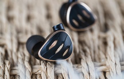 Schwarzer In-Ear-Kopfhörer mit dreieckigem Gehäuse, umrandet von roségoldenem Metall, Vorderseite mit drei kupferfarbenen Gittern, schwarzer Silikonaufsatz, in Nahaufnahme aus drei Viertel-Perspektive gesehen