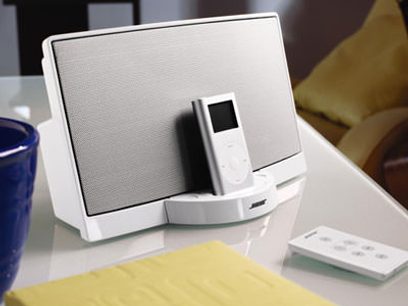 Hvid Bose SoundDock set forfra, LCD-skærm, iPod-dock, hvid fjernbetjening liggende foran på gul overflade