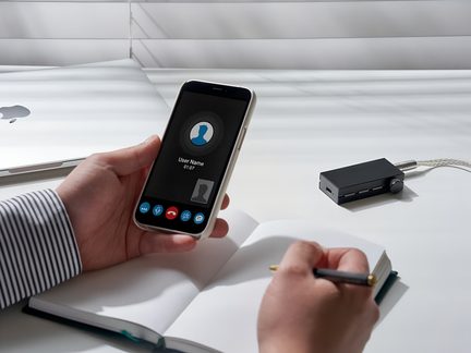 Hlavní osoba držící smartphone s displejem zobrazujícím hovor s názvem "User Name", vedle USB hubu a pera na stole