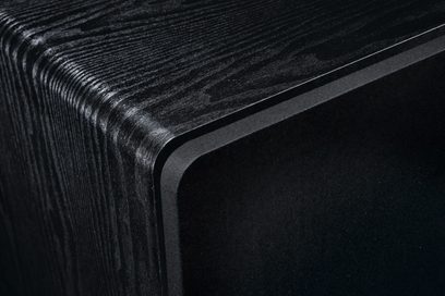 Sort Alpha RS 8 subwoofer med trætekstureret finish synlig på den afrundede øverste kant og sort frontgitter