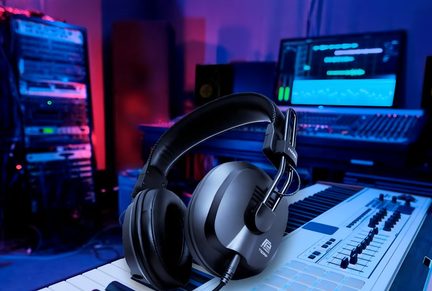 Černé sluchátko položené na bílém elektronickém klávesovém nástroji s displejem a audio vybavením v pozadí