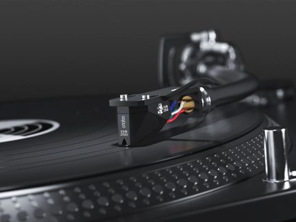 Sort phono-pickup i metal og plast, synlige flerfarvede ledninger, på sort vinylplade, nærbillede i trekvart perspektiv
