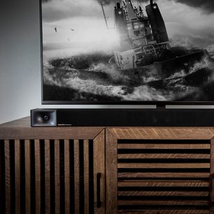 Bară de sunet Klipsch Cinema 600 din lemn închis la culoare, sub un ecran TV care afișează o imagine alb-negru a unei ambarcațiuni pe o mare agitată