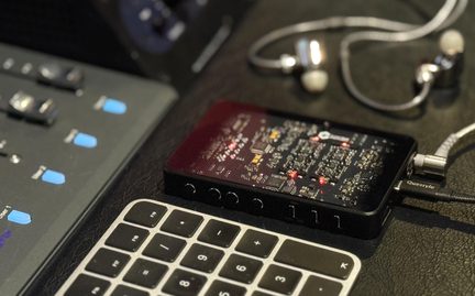 DAC amplificator de căști portabil Questyle, negru, cu capac transparent care lasă să se vadă placa de circuit imprimat, așezat lângă căști și tastatură