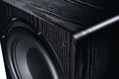 Černý subwoofer Alpha RS 8 s dřevěnou texturovanou povrchovou úpravou, pohled ze šikmého úhlu ukazující kruhový reproduktor a kovový vložku
