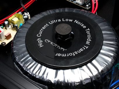 Ultra nízkošumový toroidní transformátor v černém kruhovém pouzdře s nápisy "Emotiva" a "High Current Ultra Low Noise Toroidal Transformer"