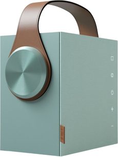 Bærbar Bluetooth-højttaler Morel Biggie i turkisblå set fra højre forfra i trekvart vinkel, kubisk kabinet i turkisblå tekstureret metal med stor børstet cirkelskive på fronten, buet håndtag i brunt læder og hvide berøringsikoner på højre side