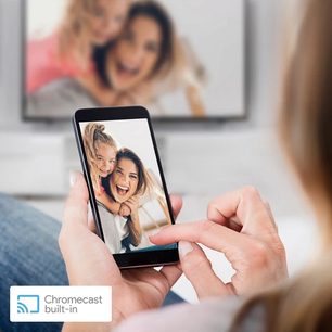 Smartphone, der viser et billede af to smilende unge kvinder, der tager en selfie, holdt i en hånd