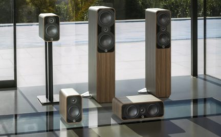 Sada hnědých hi-fi reproduktorů s dřevěným dekorem a černým předním panelem, vybavená dvěma basovými reproduktory a jedním výškovým reproduktorem, sestávající ze dvou sloupových reproduktorů, stojací knihovny, vodorovné centrální jednotky a podlahové knihovny, pohled zepředu v mírné perspektivě