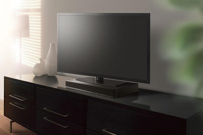Yamaha SRT-700 sort soundbar, set forfra, placeret på et mørkt træmøbel til TV, med et fjernsyn oven over