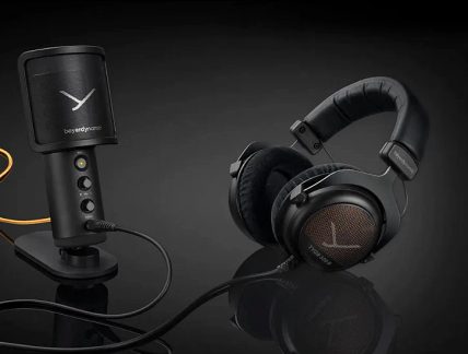 Чорний мікрофон з круглими кнопками та чорні навушники з м'якими подушечками, видимі кабелі, темне тло