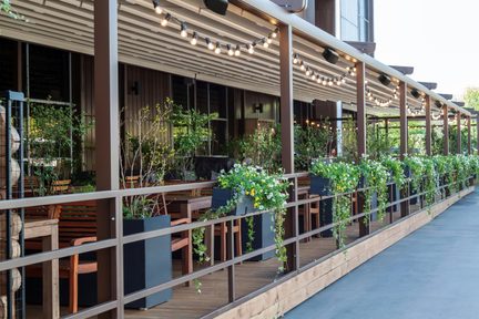 Terrazza di ristorante coperta con ghirlande luminose, fioriere fiorite e arredi in legno
