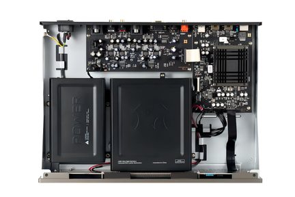 Topview af et åbent gråt metalchassis, der indeholder to sorte rektangulære plastmoduler, et stort sort printkort fyldt med elektroniske komponenter, en sort gitterformet køleplade og flere bundter af flerfarvede kabler