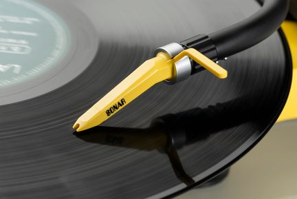 Black tonearm with a yellow head marked "SONAR," placed on a black vinyl record with visible grooves, close-up view.