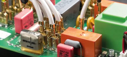 Vista ravvicinata di un circuito stampato con componenti elettronici colorati, cavi bianchi e connettori dorati