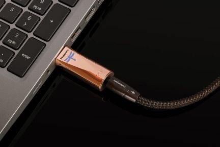 Conversor USB AudioQuest DragonFly cobre conectado a um computador portátil com cabo trançado preto e castanho