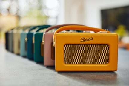 Bærbar rektangulær sennepsgul radio i tekstureret kunstlæder med buet håndtag, gylden metalgitter og relief-logo, set forfra