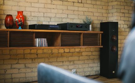 Schwarze Hi-Fi-Anlage mit Player und Verstärker auf einem Wandmöbel aus Holz, großer Standlautsprecher rechts