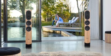 Pár světlých dřevěných hi-fi sloupových reprosoustav se třemi černými reproduktory, moderní obývací pokoj otevřený na terasu a vodní plochu