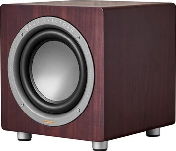 AudioVector QR Sub SE subwoofer i valnød, set fra trekvart forfra, kubisk kabinet i mørkt valnøddetræ med synlig åretegning, cirkulær højttalerenhed med grå membran omgivet af en aluminiumsring, placeret på fire cylindriske metalfødder