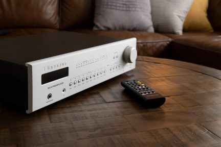 Silverfärdig Bryston BR-20 hi-fi-försteg med fjärrkontroll på ett träbord framför en soffa