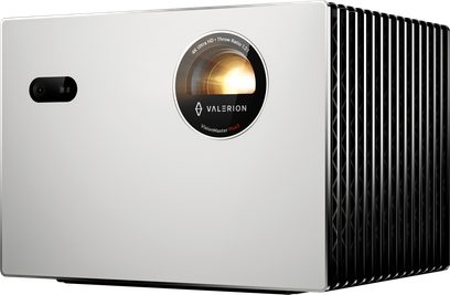Valerion StreamMaster Plus 2 matte white aluminum projector, rectangular case seen from the front right three-quarter angle, large black circular lens in the center of the front panel, small black sensor on the left, right side equipped with black cooling fins
