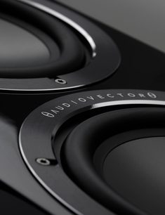 Skråt nærbillede af to sorte, cirkulære højttalerenheder på AudioVector QR7 SE gulvhøjttaleren, omgivet af mørke børstede aluminiumsringe med synlige skruer og kontrastfuldt AudioVector-logo