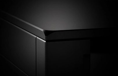 Close-up top view of a corner of the Rega Aura MC black phono preamp, showing the beveled edge of the metal enclosure