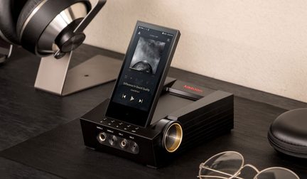 Přehrávač Astell&Kern položený na dřevěném stole, sluchátka a kabel v blízkosti, pohled zepředu s mírným nadhledem